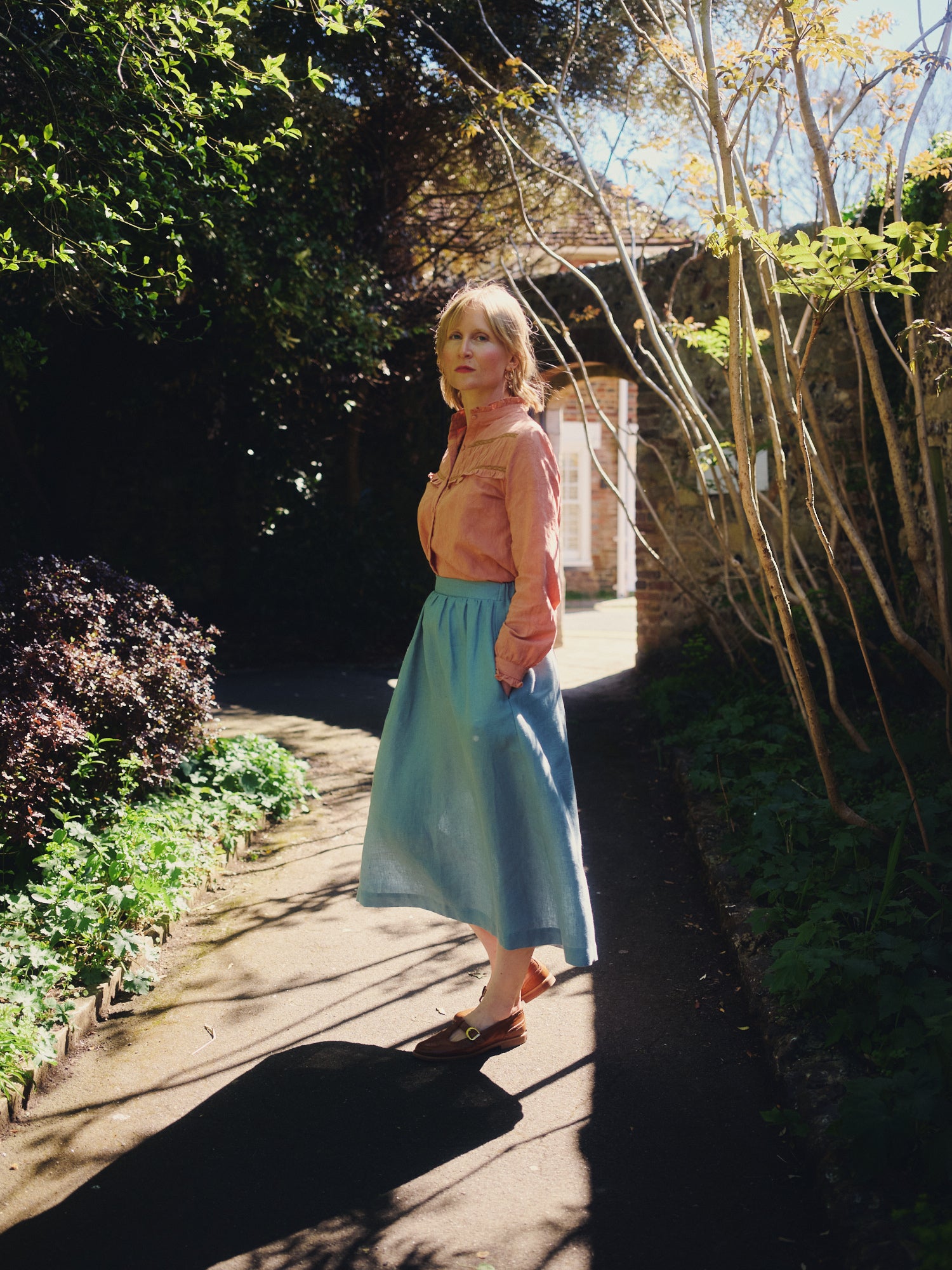 Woman in a garden wearing a pink top and blue skirt.