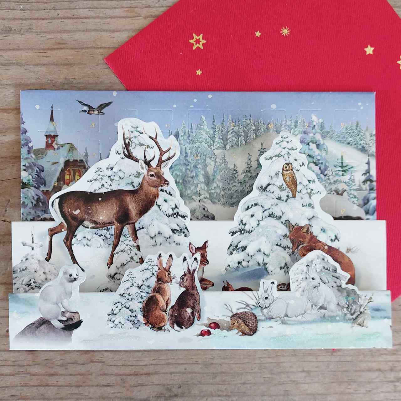 Winter scene with animals in a snowy landscape, featuring a red envelope with gold stars.
