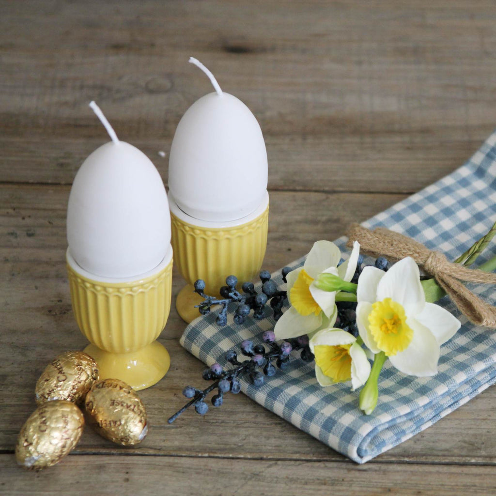 Egg Candle - White egg shaped candle with a yellow interior with egg cups and daffodils